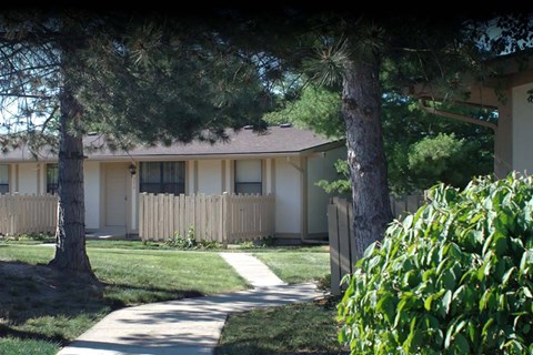 a small yellow house with a sidewalk and trees