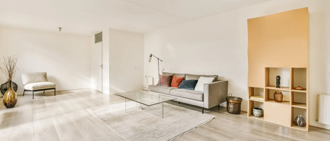 a living room with wood flooring and white walls, including a glass coffee table on the right hand side