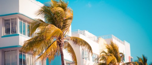 Vintage image with palm trees and a typical retro Art Deco style apartment building seen from South Beach in Miami, FL.