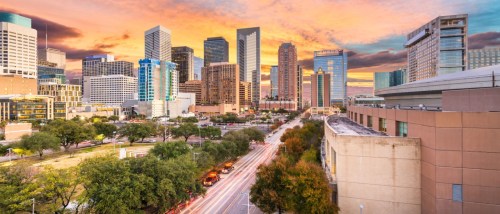 Downtown Houston skyline at sunset, featuring a mix of modern skyscrapers and lush green spaces.