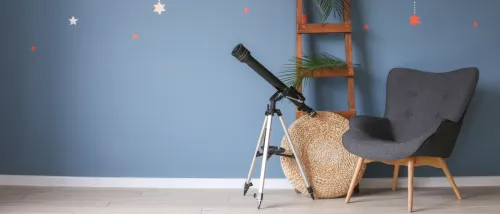 A cozy stargazing spot in a living room featuring a modern telescope on a tripod, a comfortable chair, and a blue wall adorned with star decals, creating a relaxing atmosphere for observing the night sky.