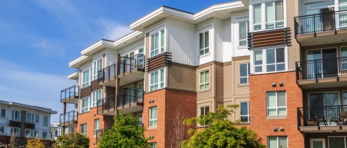 Modern suburban apartment complex with varied brick and siding façades, featuring balconies and large windows under a clear blue sky.