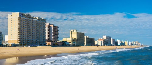 High-rise apartments along the sandy shore of Virginia Beach under a partly cloudy sky.